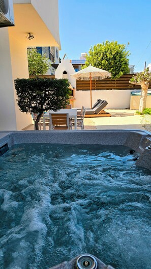 A hot tub with a stone surround, outdoor seating with a table and chairs, and a pergola with a canopy. - Villa Alkioni 31 with Private Pool & Jacuzzi (Paralimni)