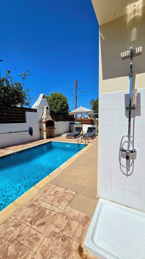Une piscine avec des chaises longues, un espace barbecue et une douche.