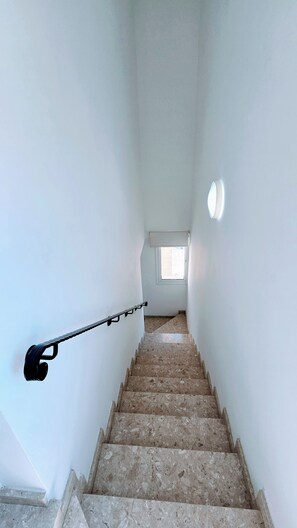 Un escalier étroit doté d’une main courante, menant à un palier avec une fenêtre.