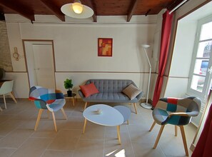 Ein Wohnzimmer mit grauem Sofa, zwei gemusterten Sesseln, einem kleinen Tisch und einer Stehlampe.