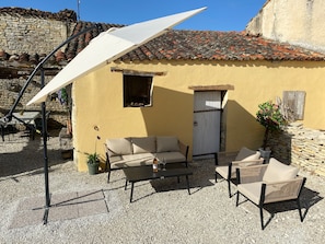 Un pati amb mobles d'exterior, un parasol blanc i una paret de pedra.