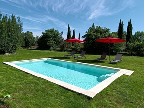 Ein rechteckiger Pool mit Fliesenrand, umgeben von einer gepflegten Rasenfläche und roten Sonnenschirmen.