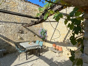 Un espacio al aire libre con pared de piedra, una mesa con sillas y plantas en macetas.
