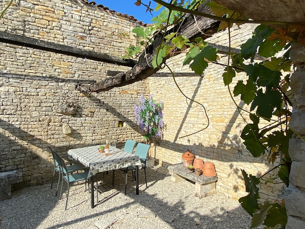 An outdoor seating area with a stone wall, a table with chairs, and potted plants.