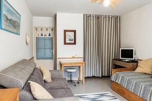 Een kleine kamer met een bank, een bureau, een bed, een televisie en een gordijn.