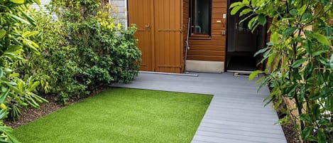 A modern building with a wooden door, a small garden with artificial grass, and a wooden deck.