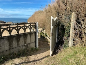 A concrete pathway leading to a beach with a metal gate. - Beachfront studio in a gated community, direct beach access, private parking (La Turballe)