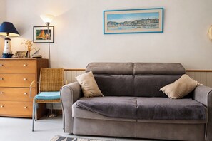 A living room with a grey sofa, a wicker chair, a wooden dresser, and a framed painting on the wall. - Beachfront studio in a secure complex, direct beach access, private parking   (La Turballe)