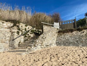 A stone staircase leading down to a sandy area with a white fence and vegetation. - Beachfront studio in a secure complex, direct beach access, private parking   (La Turballe)