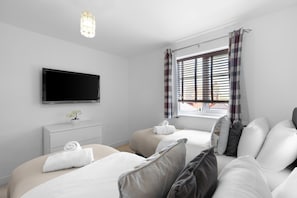 Ein Hotelzimmer mit zwei Betten, einem Flachbildfernseher, einem kleinen Topfpflanzen und einem Fenster mit Jalousien.