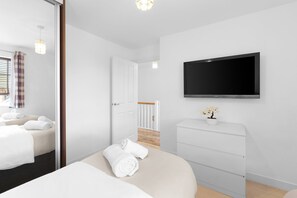 Ein modernes Hotelzimmer mit Bett, Kommode, Fernseher und einer Tür zu einem Balkon.