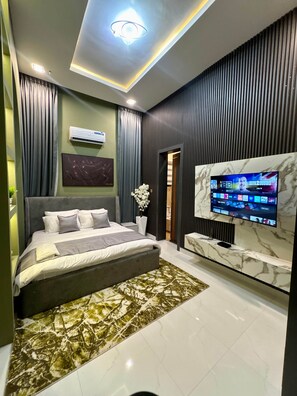 A modern bedroom with a bed, a television, and a marble wall. - Jaiye Villa Entire Place (Lekki)