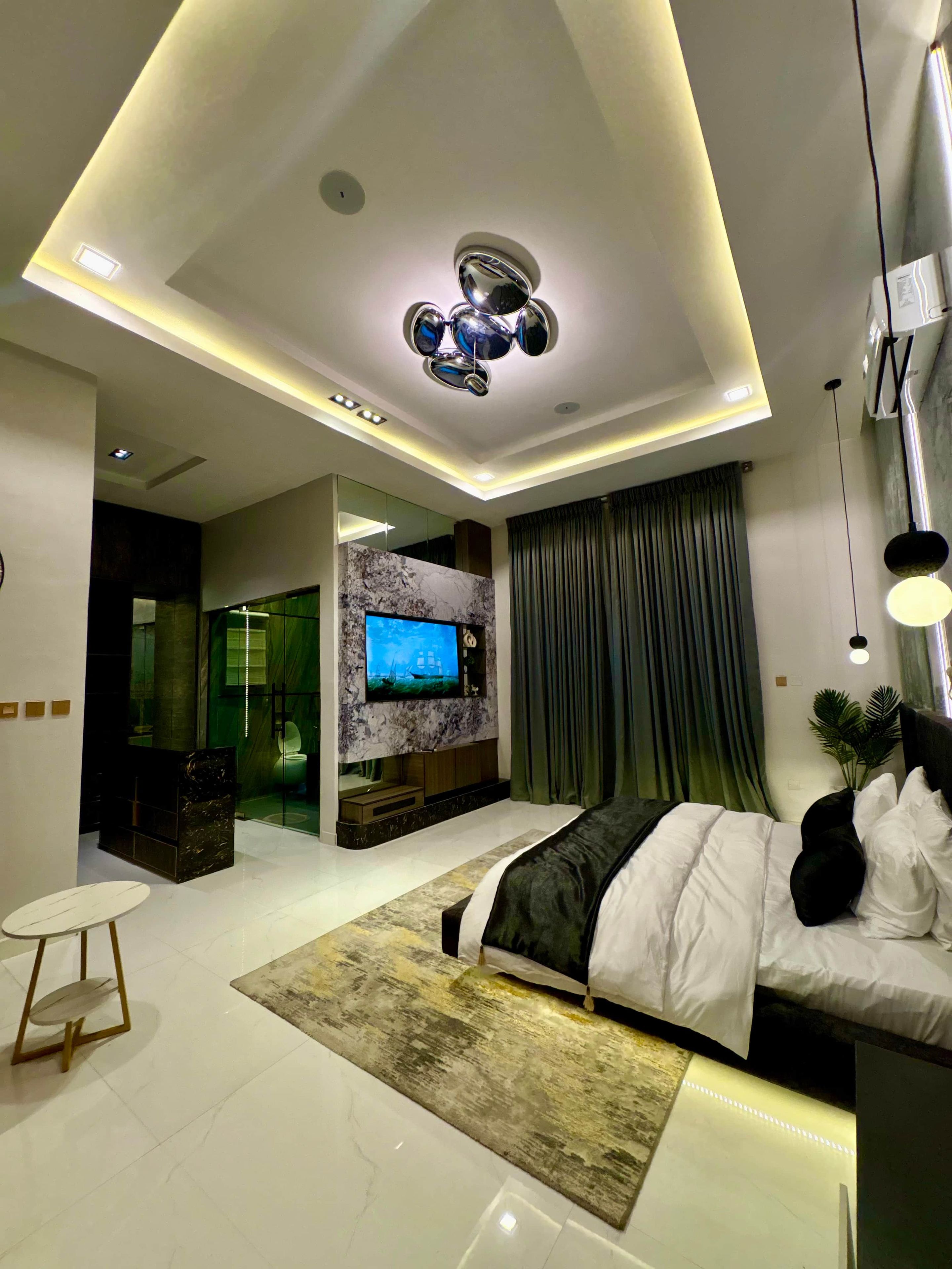 A modern bedroom with a bed, a TV, and a ceiling light fixture.