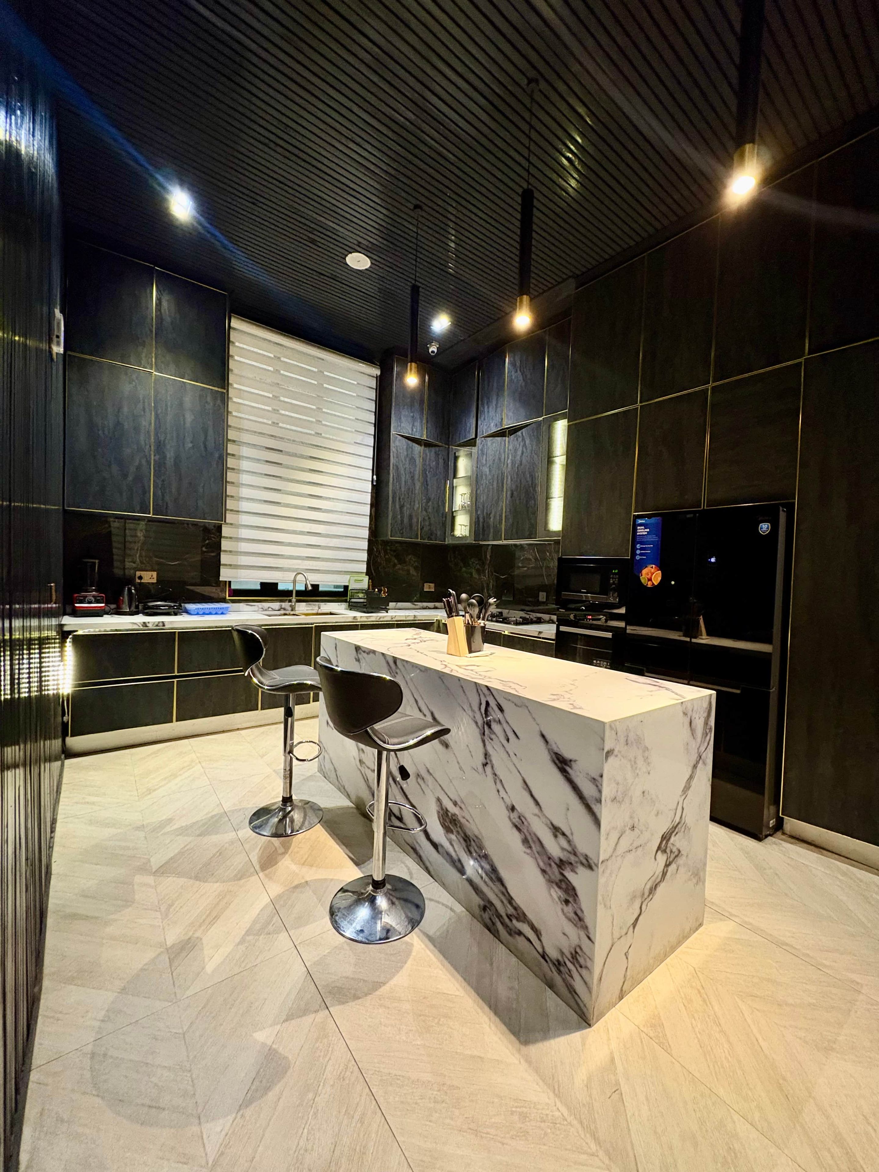 A modern kitchen with a marble island, black cabinetry, and stainless steel appliances.