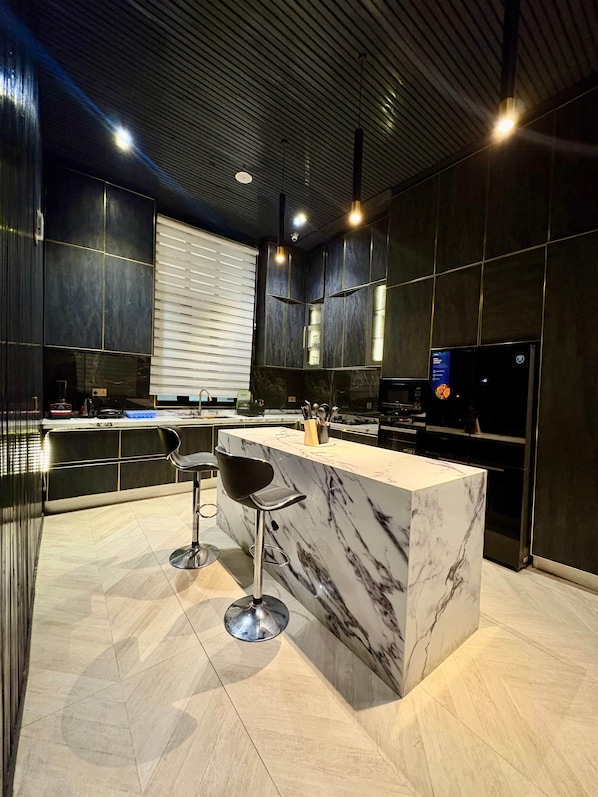 A modern kitchen with a marble island, black cabinetry, and stainless steel appliances.