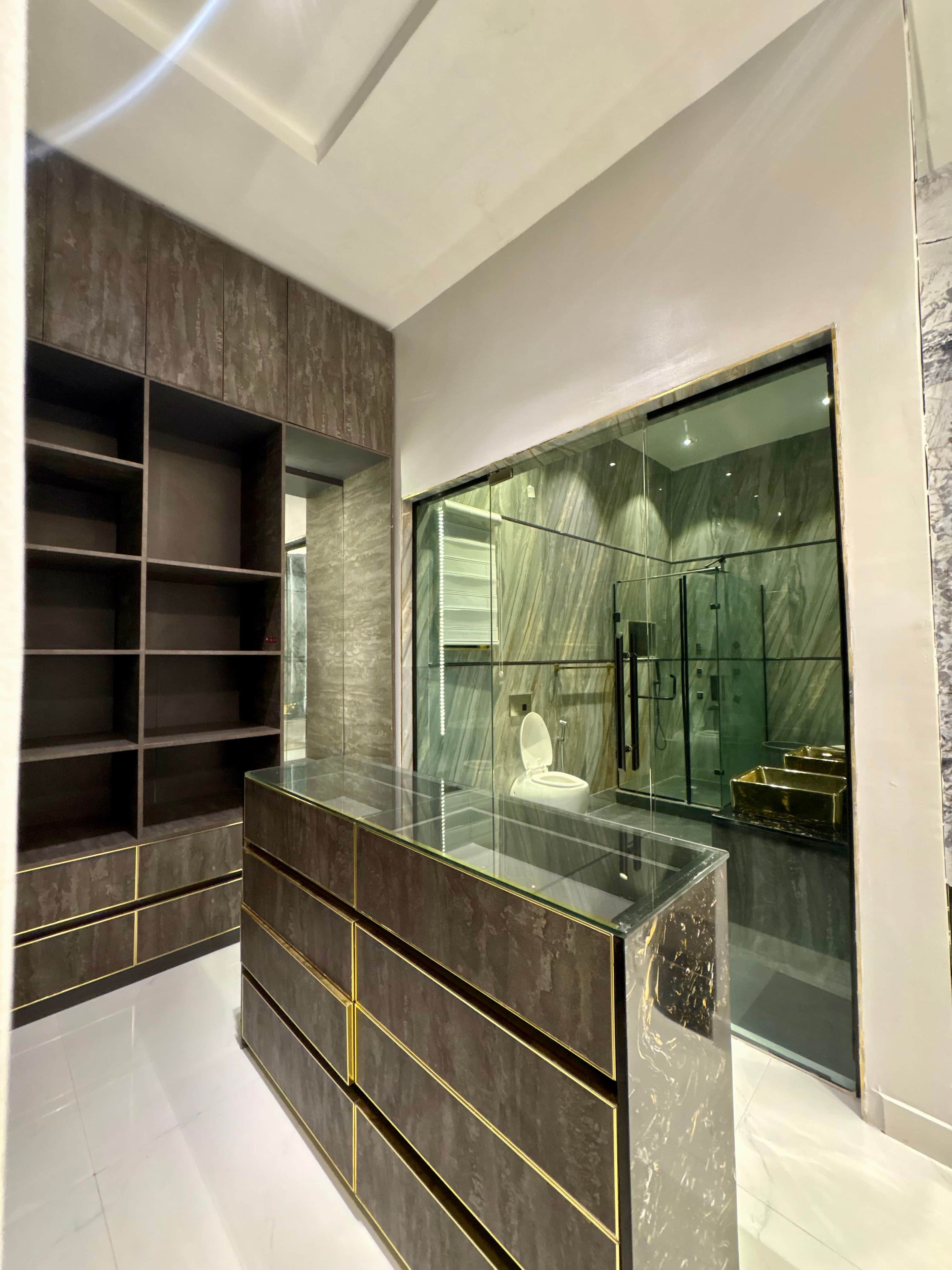 A modern bathroom with a glass-enclosed shower, marble walls, and a dark wood vanity with gold accents.