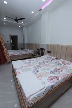 A bedroom with two beds, a ceiling fan, and a nightstand with a lamp. - Hotel Shri Ram (Agra)