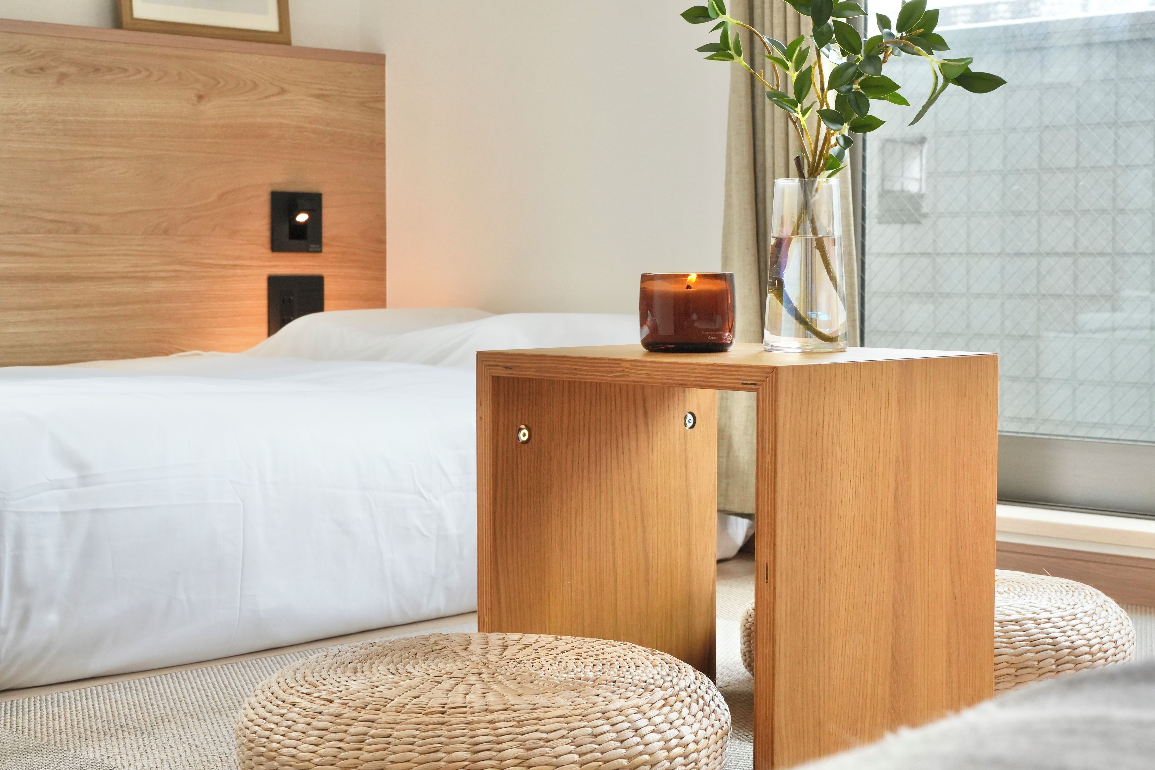 A bedroom with a wooden headboard, a bedside table with a candle, and a window with a view.