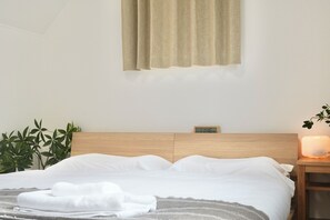 A neatly made bed with white linens and a folded towel, a bedside table with a lamp, and a plant beside the bed. - A 6-minute walk from Shinjuku-Shin-Okubo Station! 4-Bedroom, 3-Story House for Exclusive Rental (Sleeps Up to 8) | 15-Minute Walk from Kabukicho (東京都新宿区大久保二丁目)