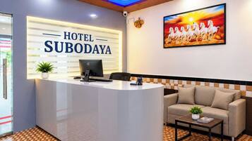 A hotel reception area with a reception desk, a computer, a sofa, and a painting of horses.