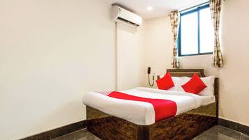 A hotel room with a bed, an air conditioning unit, a telephone, and a window with curtains.