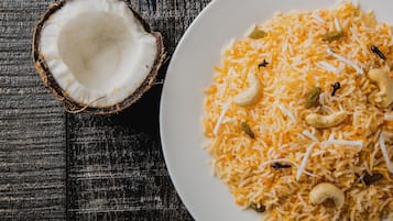 Un plato de arroz con anacardos y pasas sobre una superficie de madera oscura.