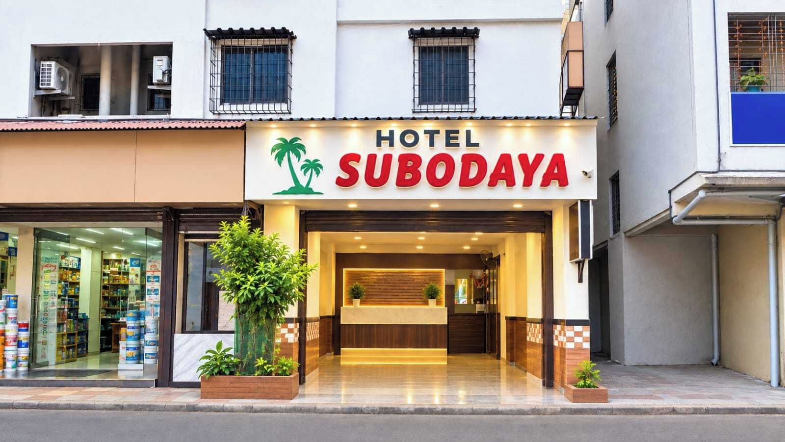 Un hotel llamado 'HOTEL SUBODAYA' con una zona de recepción, una planta visible en el exterior y un escaparate con varios artículos.
