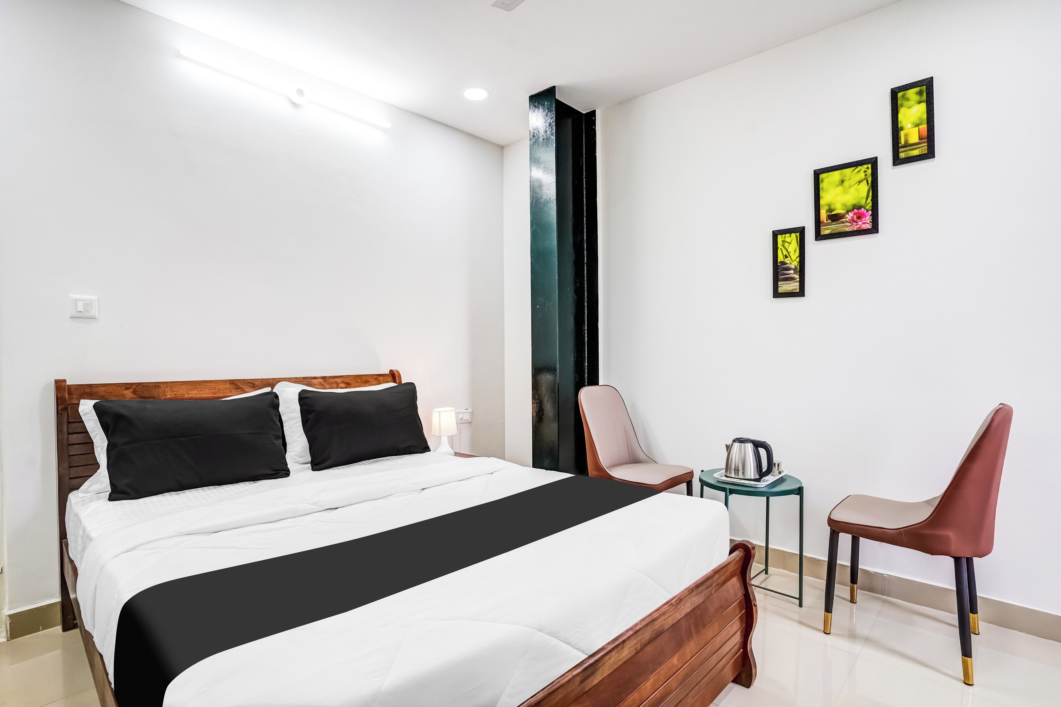 Habitación de hotel con cama, una silla, una mesa con tetera y tres cuadros en la pared.