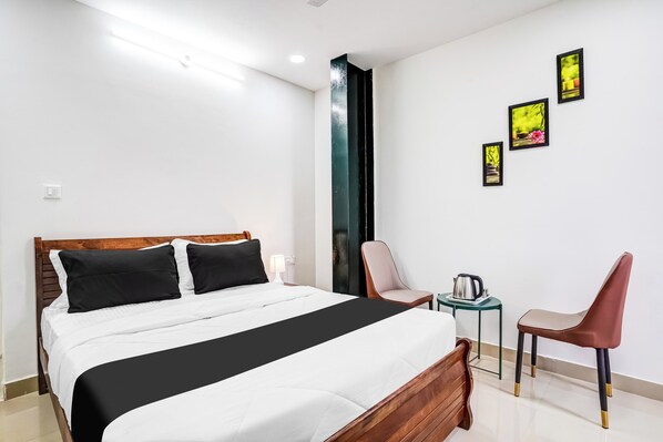 A hotel room with a bed, a chair, a table with a kettle, and three framed pictures on the wall. - Hotel O HMR Inn (Bangalore)
