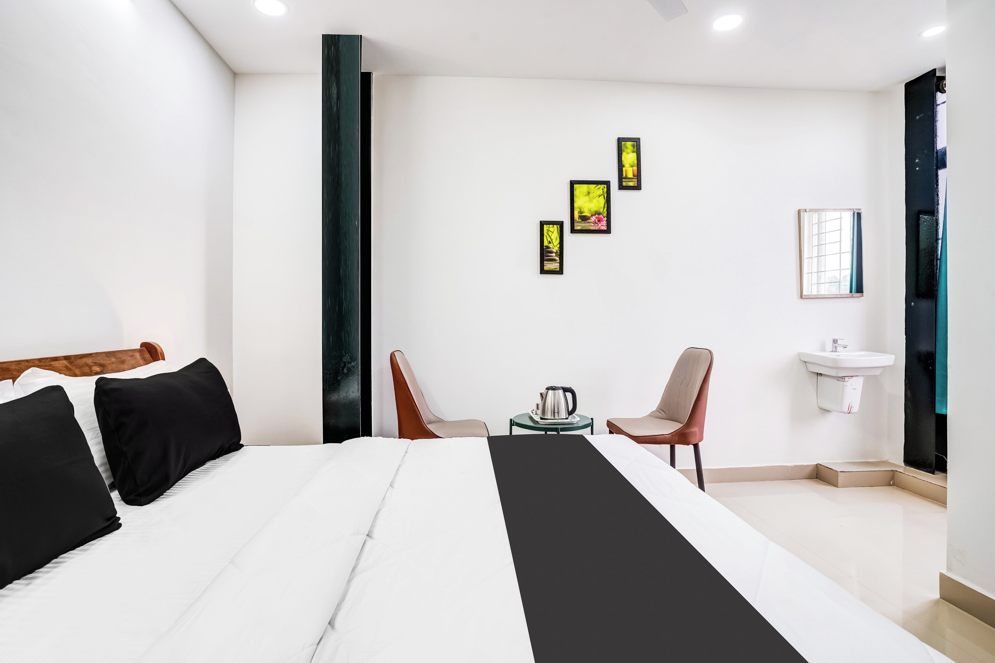 Una habitación de hotel con una cama, dos sillones, una mesita con una tetera, un lavamanos y tres cuadros en la pared.