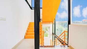 Un interior moderno con una escalera, un ventanal con vistas a zonas verdes y una barandilla naranja brillante.
