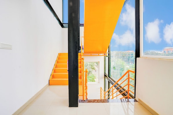 A modern interior with a staircase, a window with a view of greenery, and a bright orange safety rail.