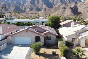A residential area with houses featuring red-tiled roofs, a white garage, and a landscaped front yard with shrubs and a small tree. - La Quinta Cove Oasis | Private Pool & Mountain Views (La Quinta)