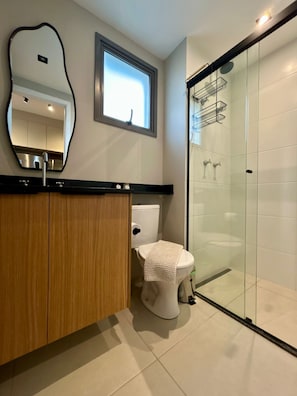 A modern bathroom with a wooden vanity, a toilet, a glass shower enclosure, and a large mirror. - Level Brooklin 1217 (São Paulo)