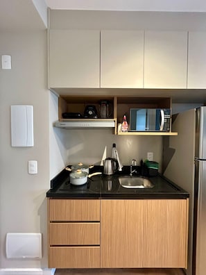 A compact kitchen with a microwave, kettle, and a small shelf above the counter. - Level Brooklin 1217 (São Paulo)