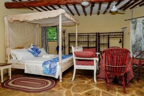 Ein Zimmer mit einem Himmelbett, einem Korbstuhl und einem roten karierten Sessel.
