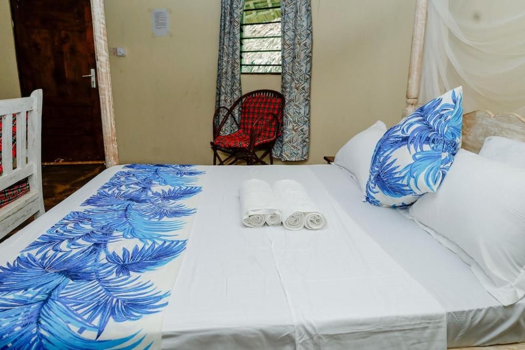 A bed with white linens, a red chair, and a window with patterned curtains.