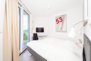 A modern hotel room with a large bed, a television, a desk, and a sliding glass door to a balcony. - Dune Villa 02, Apartment 02 (Lübeck-Travemünde)