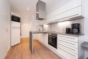 Een moderne keuken met witte kastjes, een inbouwoven, een koffiezetapparaat en een magnetron.