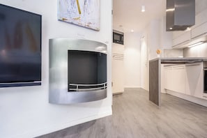 A modern kitchen with built-in appliances, a flat-screen TV mounted on the wall, and a wooden floor. - Dune Villa 02, Apartment 02 (Lübeck-Travemünde)