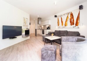 A modern living room with a flat-screen TV, a fireplace, a grey sofa, and a dining table. - Dune Villa 02, Apartment 02 (Lübeck-Travemünde)