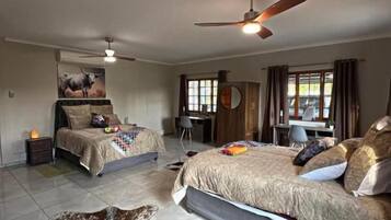 A bedroom with two beds, a ceiling fan, a desk, and a large rug.