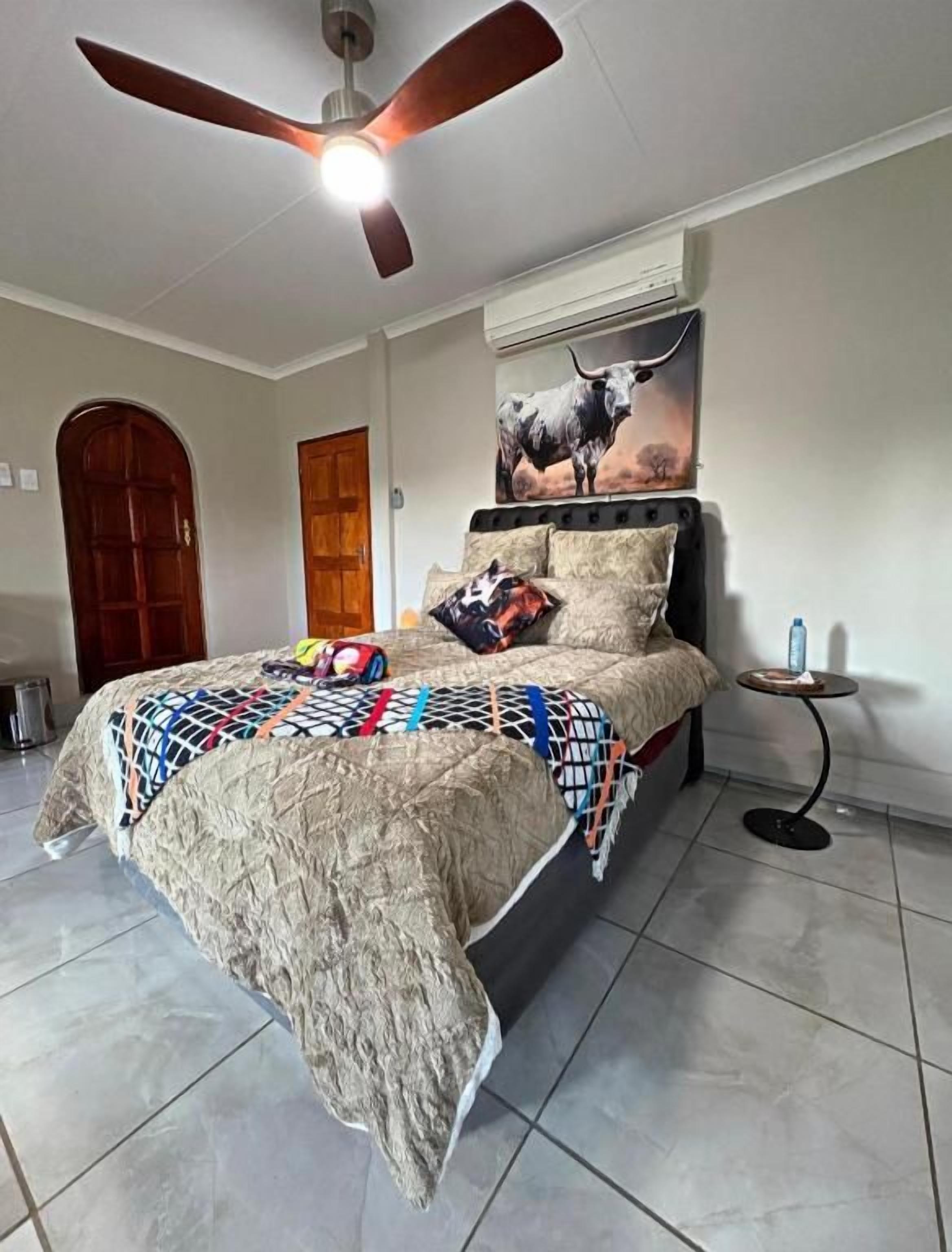 A bedroom with a bed, a ceiling fan, a wall-mounted air conditioner, a door, and a small table with a bottle.