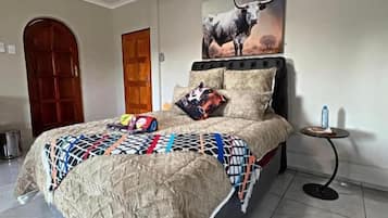 A bedroom with a bed, a ceiling fan, a wall-mounted air conditioner, a door, and a small table with a bottle.
