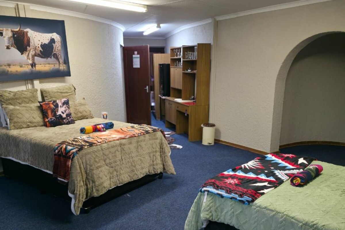 Una habitación con dos camas, un cuadro de toro colgado en la pared, una puerta que da a otra habitación y un gran tapete de cuero de vaca.