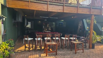 An outdoor seating area with wooden tables and chairs, a pool table, and a balcony with a wooden railing.