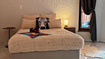 Un dormitorio con cama, mesita de noche, lámpara, ventana con cortinas y piso de baldosas.