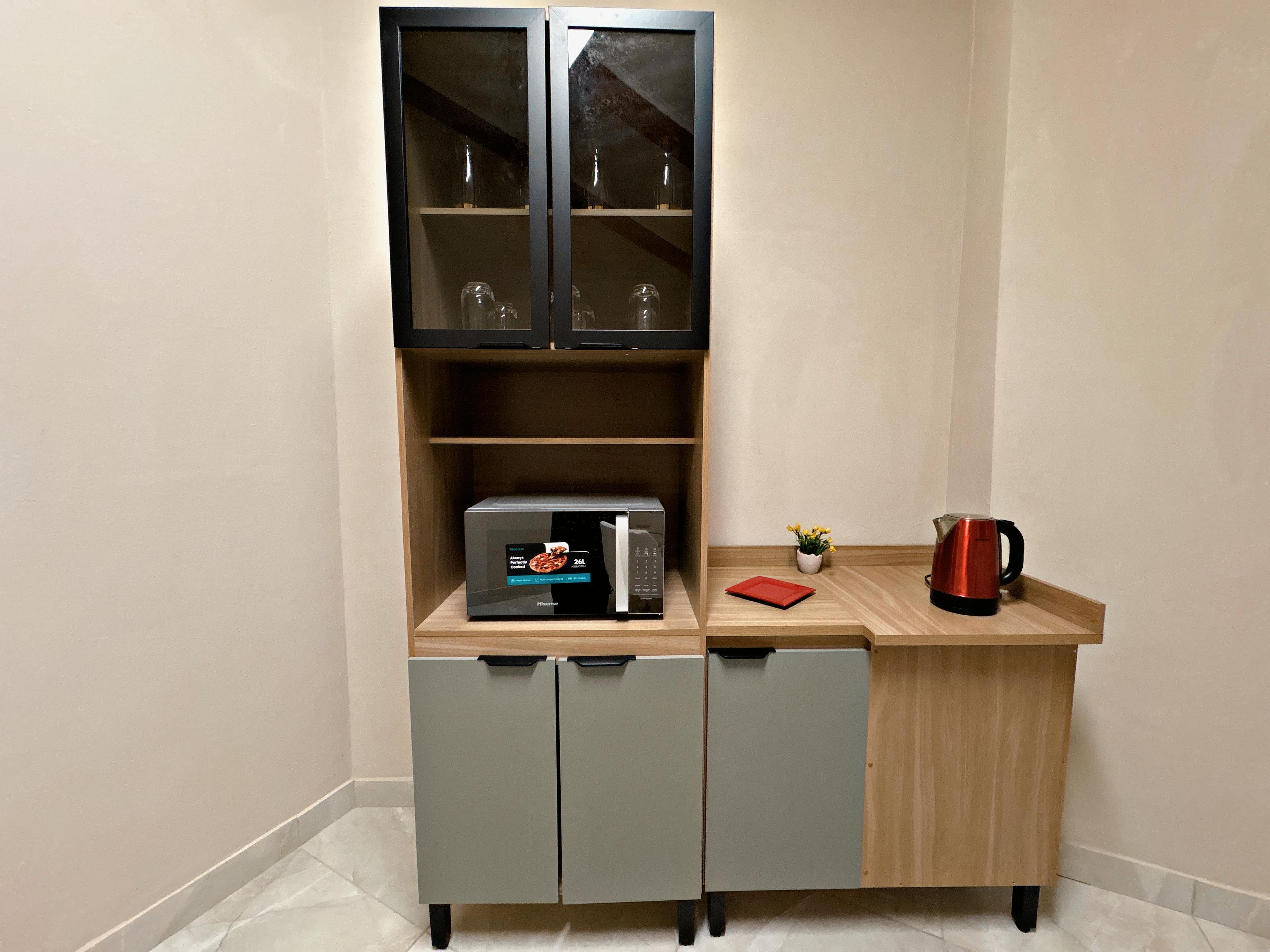 Uma cozinha compacta com micro-ondas, um armário pequeno e um tabuleiro vermelho.