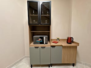 Una kitchenette con un microondas, un mueble pequeño y una bandeja roja.