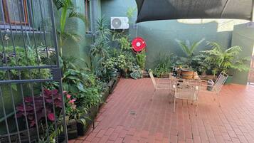A patio area with a metal table and chairs, surrounded by potted plants and a green wall.